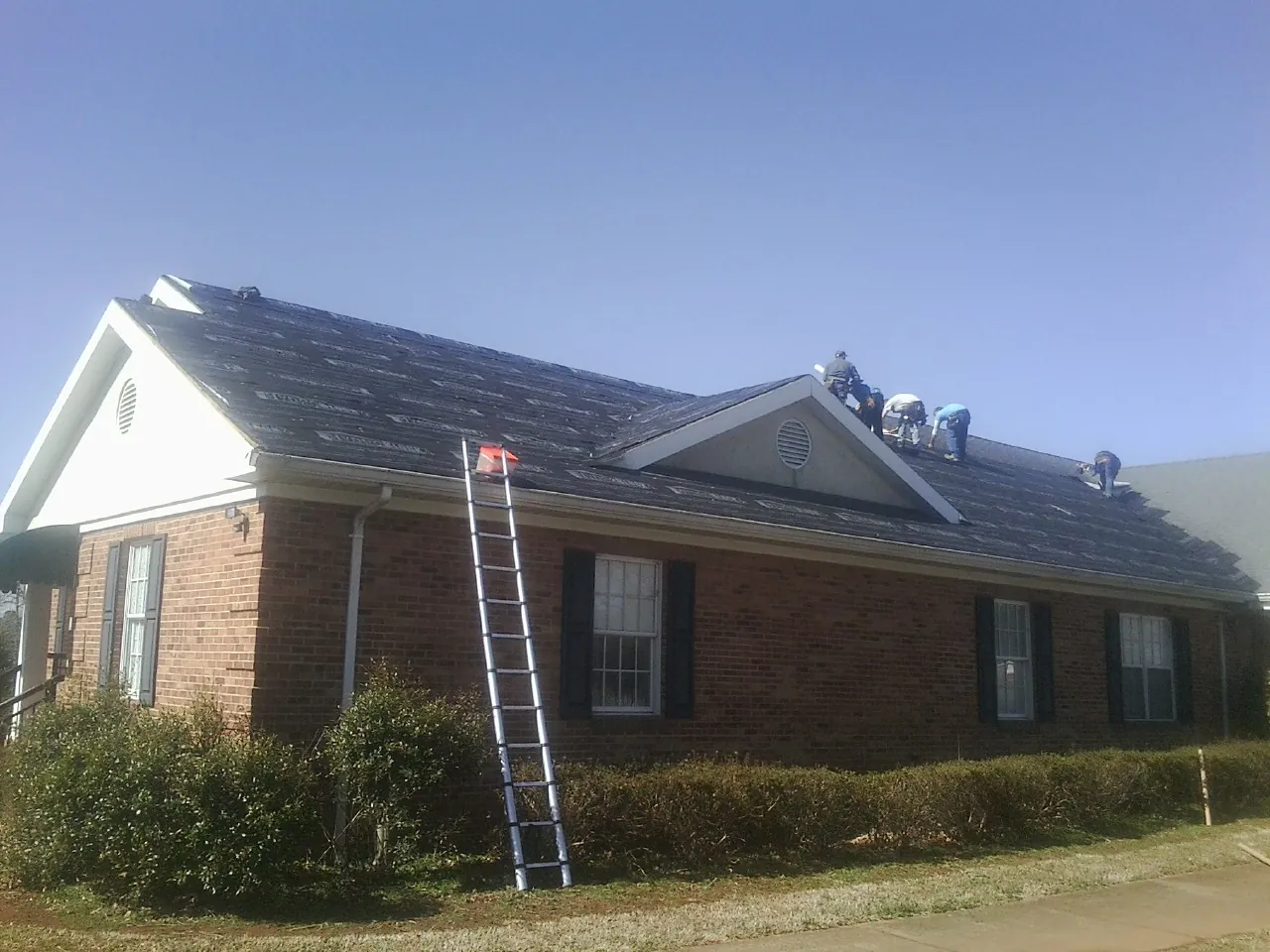 Crew tearing shingles off a brick ranch roof with a ladder set — Emergency Roof Repair work by our crew in Hungerford