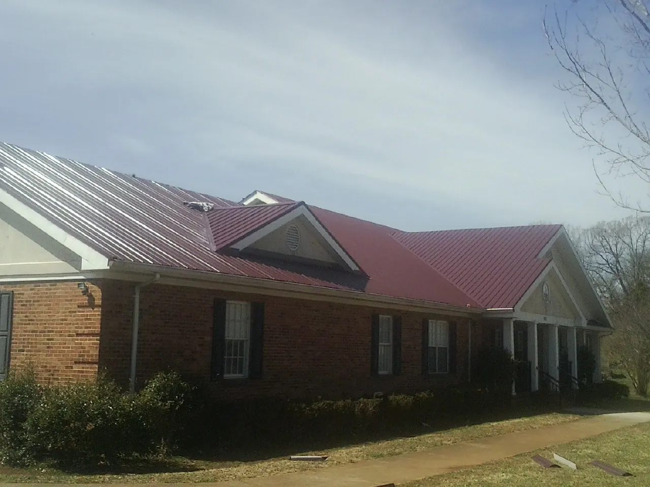 Red metal roof with gabled entries on a long brick building, from a Hail Damage Roof Repair job in Hungerford