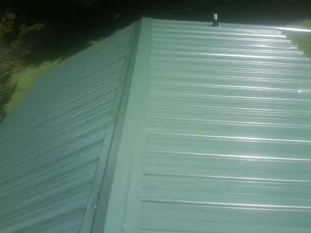 New green metal panels meeting at the ridge of a roof — Flat Roof Repair work by our crew in Hungerford