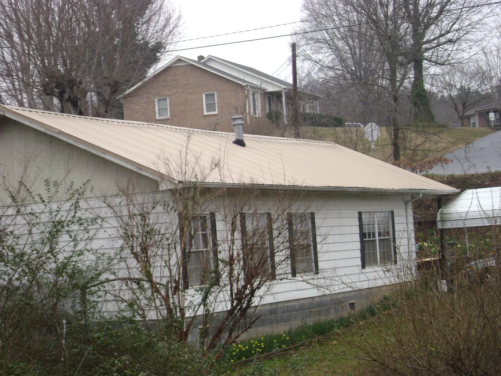 Tan metal roof on a white sided house set into a hillside — Commercial Roofing by Roofing Brothers in Hungerford